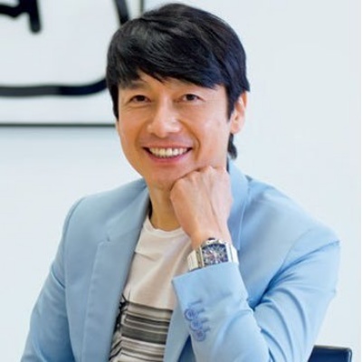あごに手を当ててはにかむ熊谷正寿